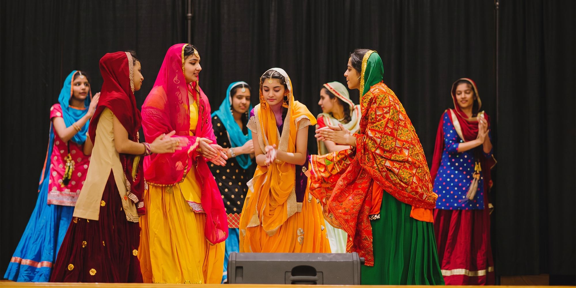 Students in bright traditional dress performing on stage at the Mother Language Day showcase.